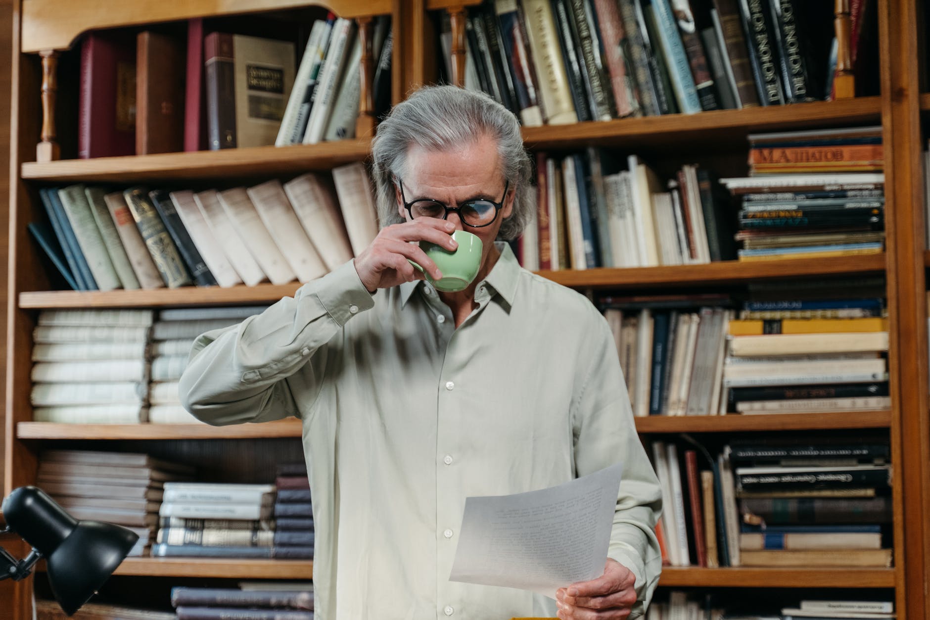 a elderly man drinking on a ceramic cup while reading a document