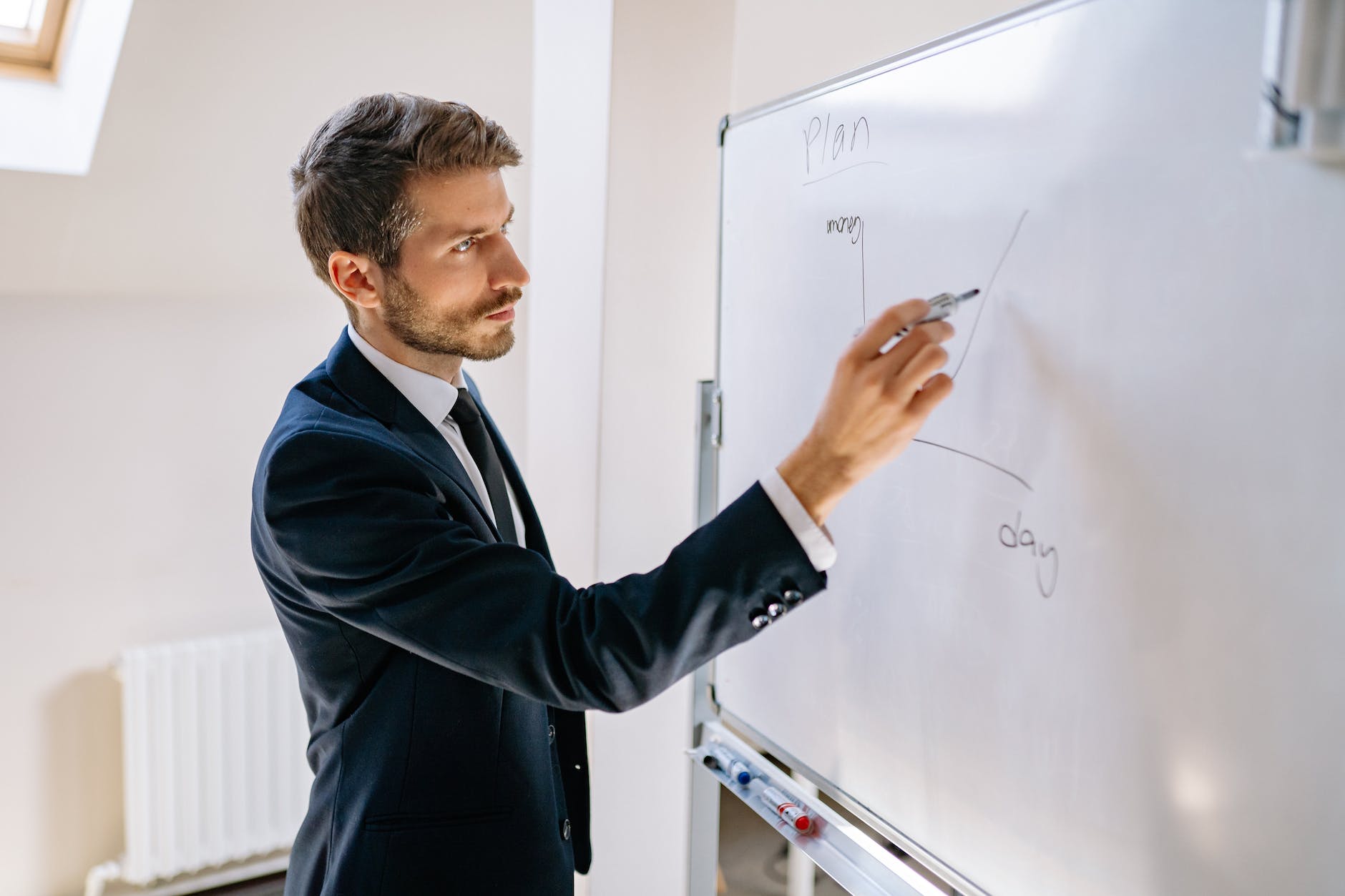 a man in corporate attire drawing a graph on a white board